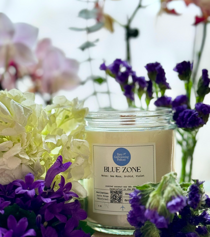 Unlit Blue Zone candle surrounded by rich purple and white flowers