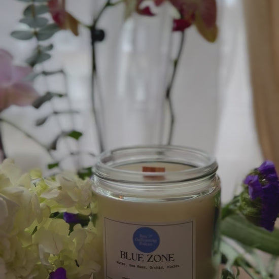 Video of someone lighting a Blue Zone candle by a windowsill, surrounded by flowers