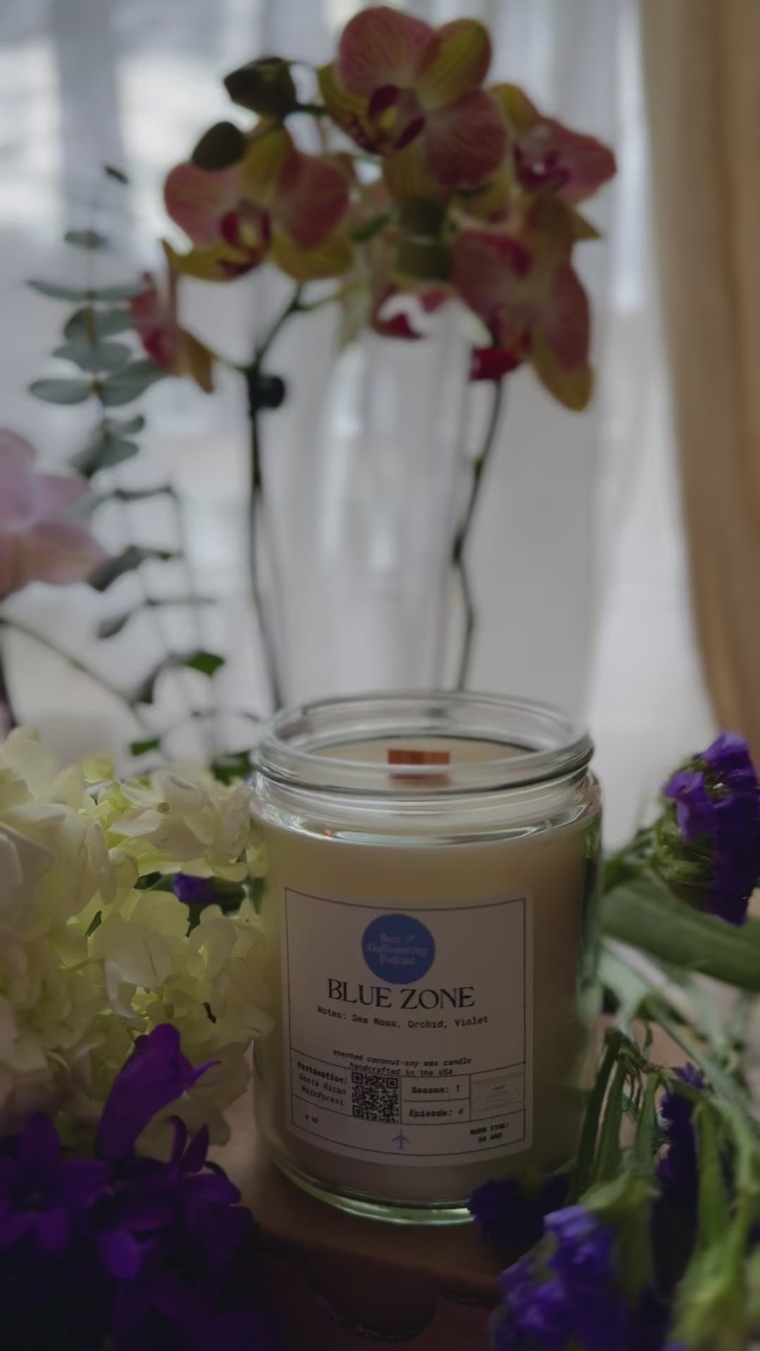 Video of someone lighting a Blue Zone candle by a windowsill, surrounded by flowers